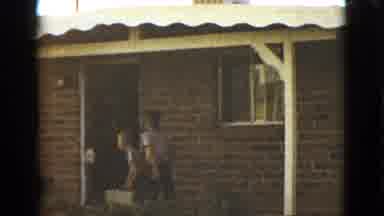 Clarksdale Arizona (1968): Boy Wearing White Plaid Shirt Carries Grey Box Into Red