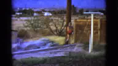 Clarksdale Arizona (1968): Boy Wearing Blue Shorts Runs To Brown Wooden Post On A