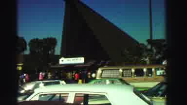 Reno Nevada (1969): A Shopping Area With Lots Of Vehicles And An American Flag