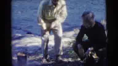 Miami Florida (1956): Two Men Squatting Down In Front Of An Outdoor Campfire Cuts