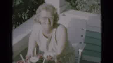 Clarkdale Arizona (1966): Woman Sitting In Porch Smiling And Smelling Flowers On A
