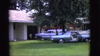 Clarkdale Arizona (1966): Woman Walks Across Lawn Past Cars Toward House And Waves