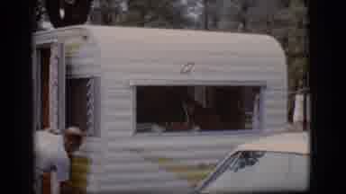 Flagstaff Arizona (1968): Man Working On Door Of Small Camper At A Wooded Campsite