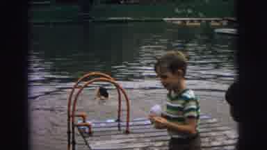 Superior Wisconsin (1973): Kid Feeding The Ducks On A Lake Near Other Kids