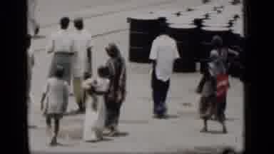Bombay India (1946): People Walking Past Black Barrels On A Bright Sunny Day