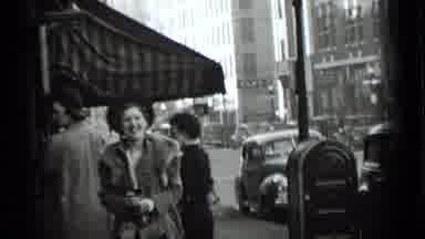 New York USA (1939): Man Wearing Grey Suit Walks Past Three Grey Cars On A Clear