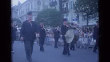 Cannes France (1962): Band Marches Along A Street While Spectators Crowd Against A