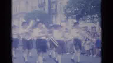 Cannes France (1962): A Marching Band Walks Down The Street Playing Instruments As