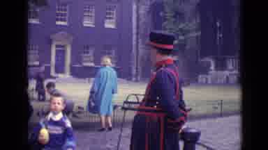 London England (1962): Three Children Rush By As Adults Stand By And Look On