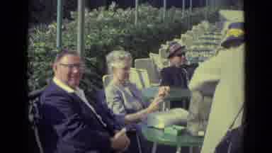 Venice Italy (1962): Woman Wearing Tan Jacket Talks To Couple Seated At Table On A