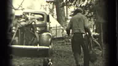 Bend Oregon (1937): A Man Followed By A Dog Carries A Bag To A Truck While Men At