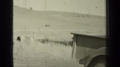 Bend Oregon (1937): A Woman In A Dress Walking Toward A Man Fixing A Truck