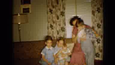 Minnesota USA (1958): Woman Wearing Red Dress Sits On Arm Of Red Sofa Hugging Boy