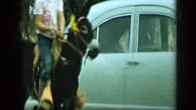 Aledo Texas (1959): Person Wearing Blue Pants Rides Burro Down Street On A Sunny