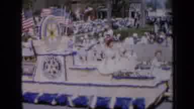 Iowa USA (1959): People In Floats Being Pulled By Cars Going Down A Street During