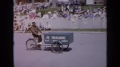 Iowa USA (1959): An Old Man Cycling His Products To Be Sold To The Crowds Watching