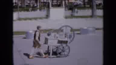 Iowa USA (1959): Man Pushing Cart Large Wheels Woman In Uniform Walking In Front