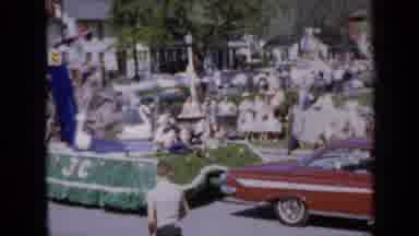 Iowa USA (1959): Boy Watches Float With Circling Swans Continue Down Street During