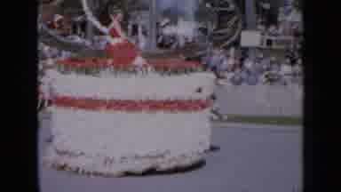 Iowa USA (1959): Woman Wearing Red Dress Sits On Top Of Red And White Parade Float