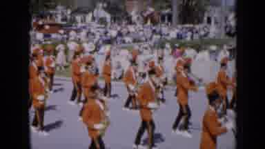 Iowa USA (1959): Marching Band In Festival Marching Down Road As Crowd Watches