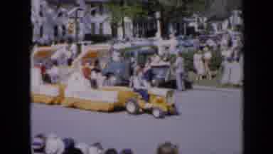 Iowa USA (1959): A Person Driving A Tractor Down The Street Pulling Two Floats In