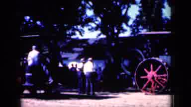 Iowa USA (1959): Men Outside Watching An Old School Tractor Ride Pass So They Can