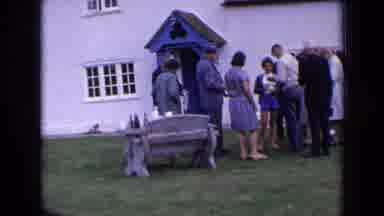 England (1963): Terrier Dog Walks Away From The Group Of People Standing Outside
