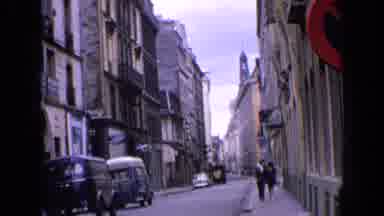 England (1963): Man And Woman Stroll Along Main Street In The City On A Crisp
