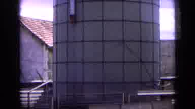France (1963): Group Of Men Standing By Stone Building Next To Grey Checked Silo