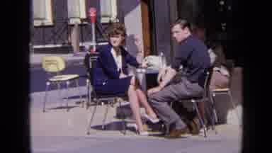 London England (1963): Woman Wearing Blue Suit Sits At Table With Man Wearing