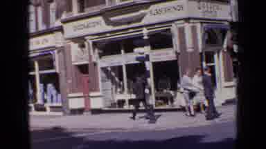 London England (1963): Man Wearing Grey Suit Walks Past Shops On A Sunny Day