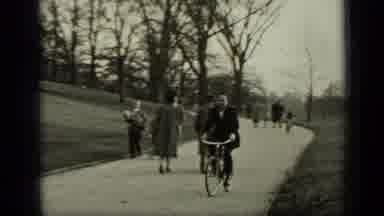 New York (1949): Man Wearing Black Coat Rides Bicycle On Sidewalk On A Clear Day