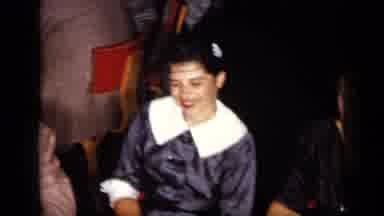 New York (1957): Woman Wearing Grey Dress And White Hair Ornament Sits At Dining