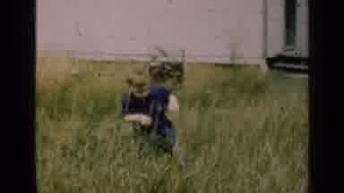 Illinois USA (1947): Little Boy Wearing Blue Walking In Tall Grass With House In