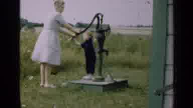 Illinois USA (1947): Woman And Child Standing By A Hand Pump In A Grassy Field