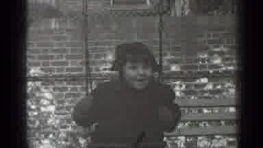 New York (1947): Girl Wearing Black Coat Swings On Swing In Front Of Brick