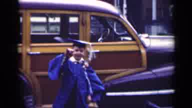Indiana USA (1948): Boy In Blue Graduation Cap And Gown Waves At Camera And Walks