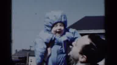 New York (1950): Man Wearing Tan Coat Hugs Baby Wearing Blue Coat On A Bright