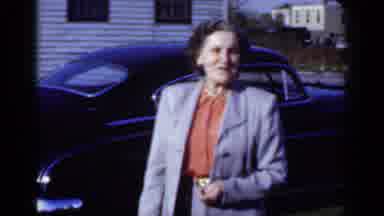 New York (1950): Woman Wearing Grey Suit Walks Past Black Car On A Bright Sunny