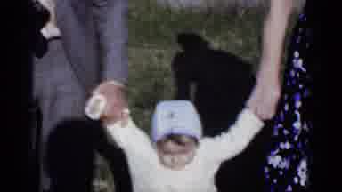 New York (1950): Couple Helps Toddler Wearing White Sweater To Walk On A Bright