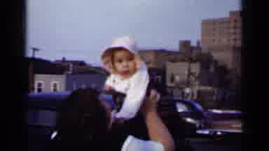 New York (1950): A Woman Holds Up A Baby Who Is Wearing A Bonnet