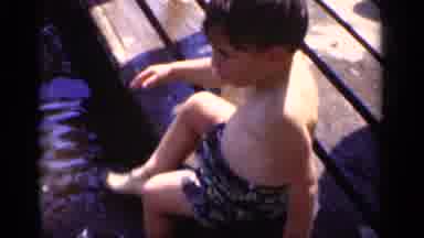 New York (1951): Boy Wearing Black Shorts Sits On Wooden Pier With Feet In Water