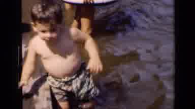 New York (1951): Boy Wearing Tan Shorts Walks In Water Next To Wooden Pier Beam On