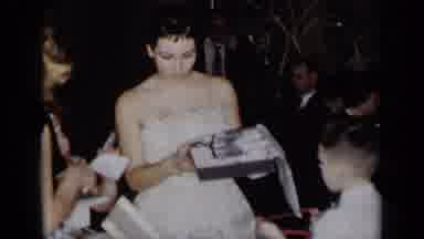 New York (1954): Woman In White Lace Dress Holds Up Gifts For The Camera And To
