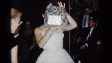 New York (1954): Bride Wearing White Dress Holds Up A Present While Surrounded By