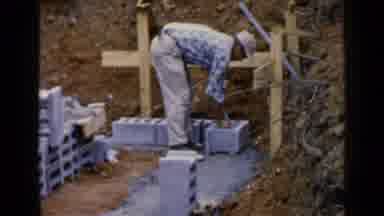 Birmingham Alabama (1957): Man Wearing Tan Pants Places Grey Bricks In Row On A