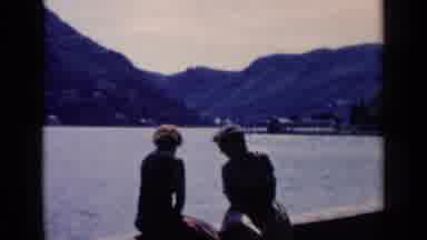 Venice Italy (1960): Couple Sitting On Concrete Ledge By Water On A Sunny Day