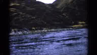 Idaho USA (1963): Fast River Flows Along Hilly Terrain With Bushes And Rocky