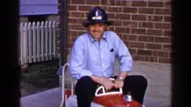 Long Island New York (1965): Man Wearing Blue Shirt Tries Riding In Red Toy Fire