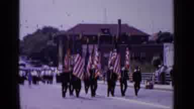 Mineola New York (1966): People Marching Down The Road With Flags As People Follow